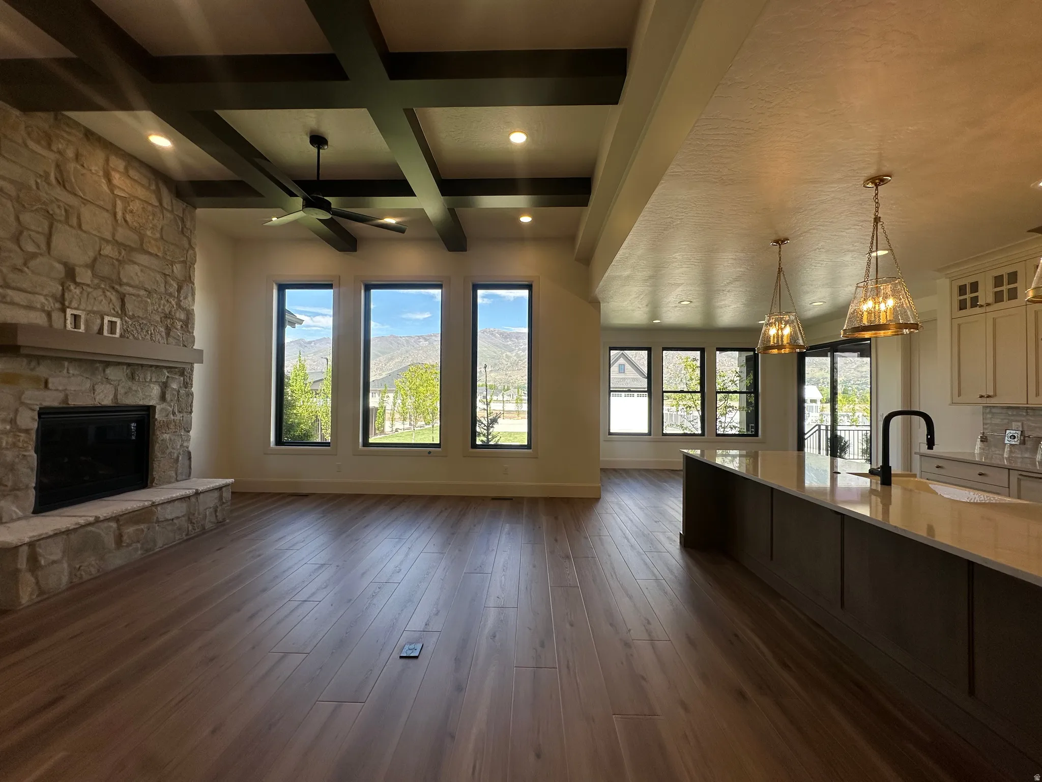 Expansive open-concept living area featuring a stone fireplace, wood-finish flooring, and coffered ceilings with recessed lighting