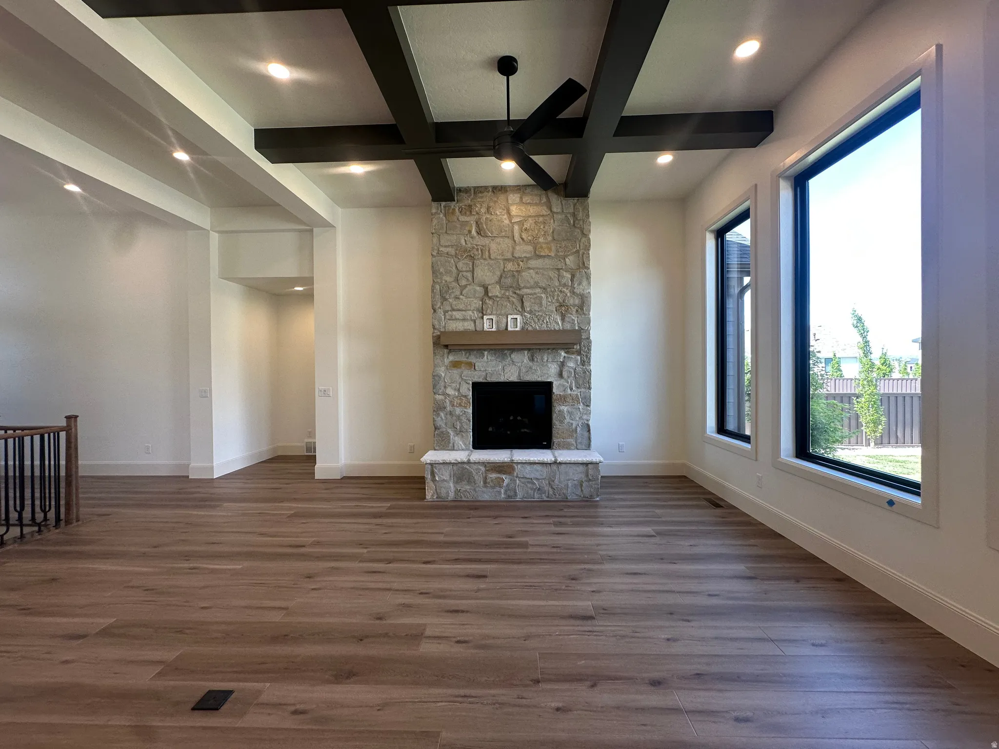 Spacious room with wood-finish flooring, a stone-clad fireplace with a wood mantle, and stained ceiling beams