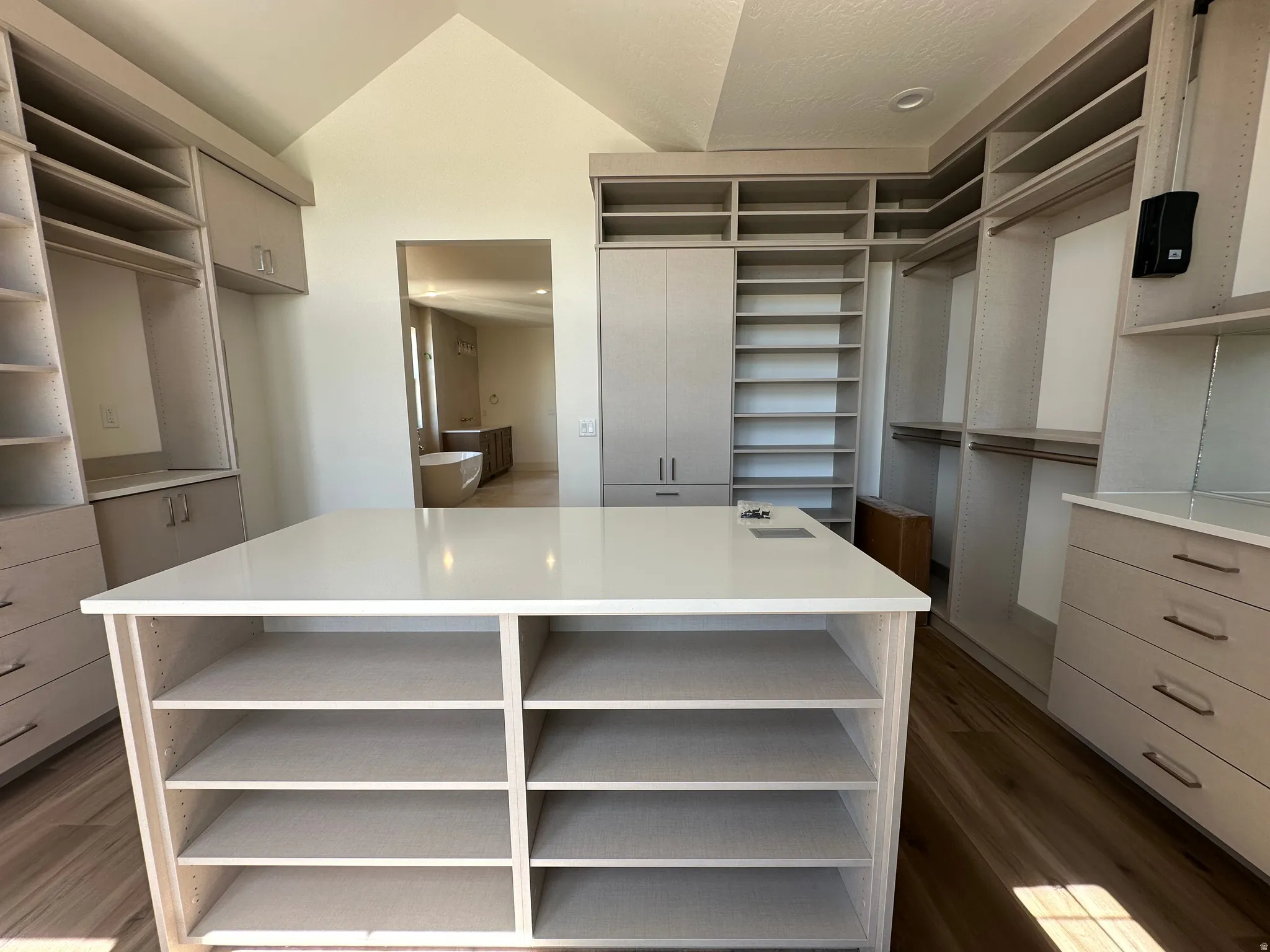 Expansive primary custom closet featuring an oversized central island with a solid surface countertop, extensive built-in shelving, multiple hanging rods, and integrated drawer storage