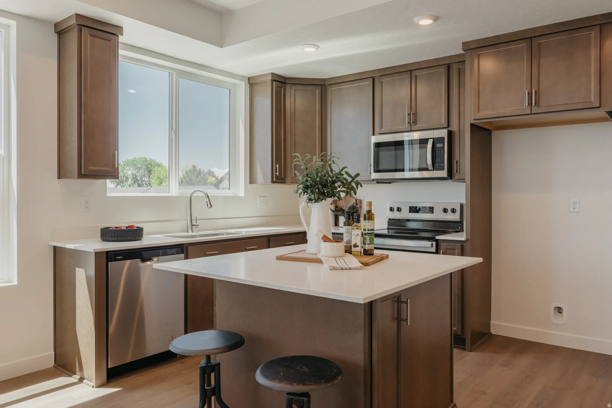 Kitchen with stainless steel appliances, light wood-style flooring, a center island, light stone countertops, and a kitchen bar