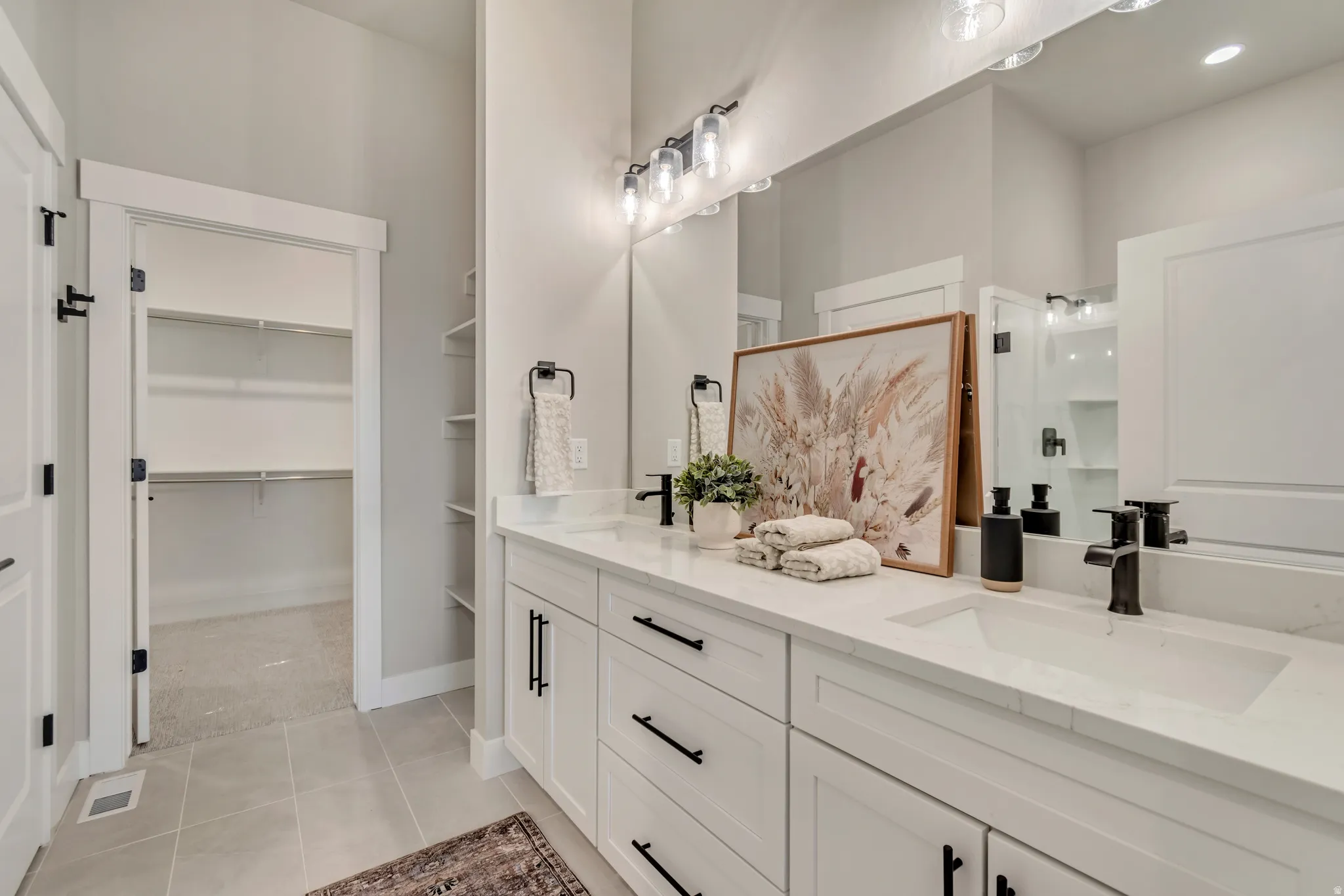 Full bathroom featuring a shower stall, double vanity, a spacious closet, and light tile patterned floors