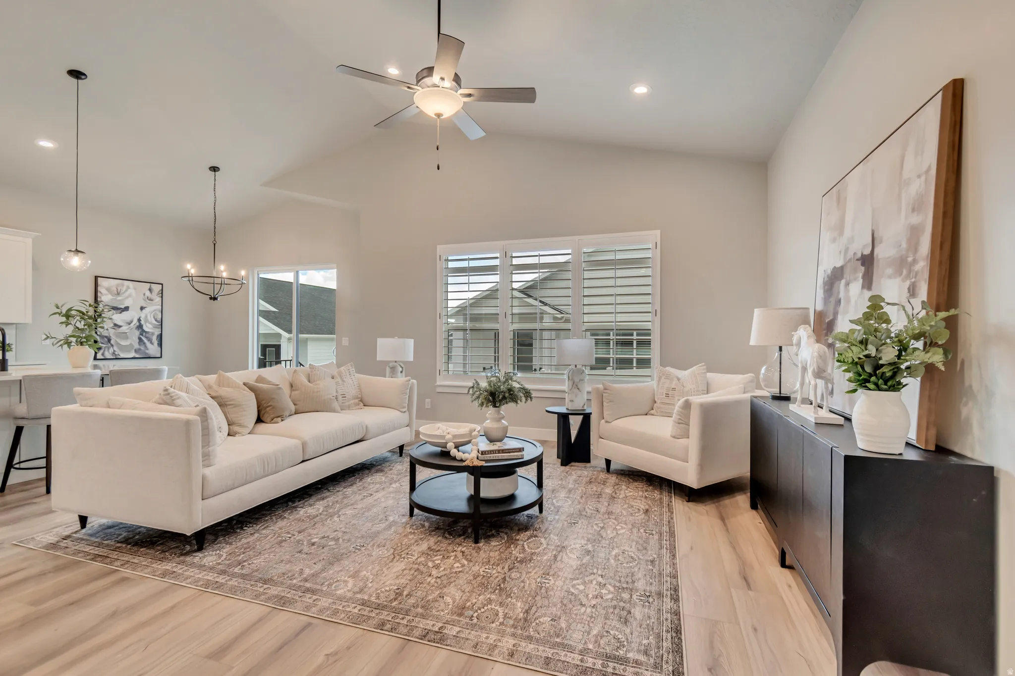 Living room featuring a ceiling fan, vaulted ceiling, light wood-style flooring, and hanging lights