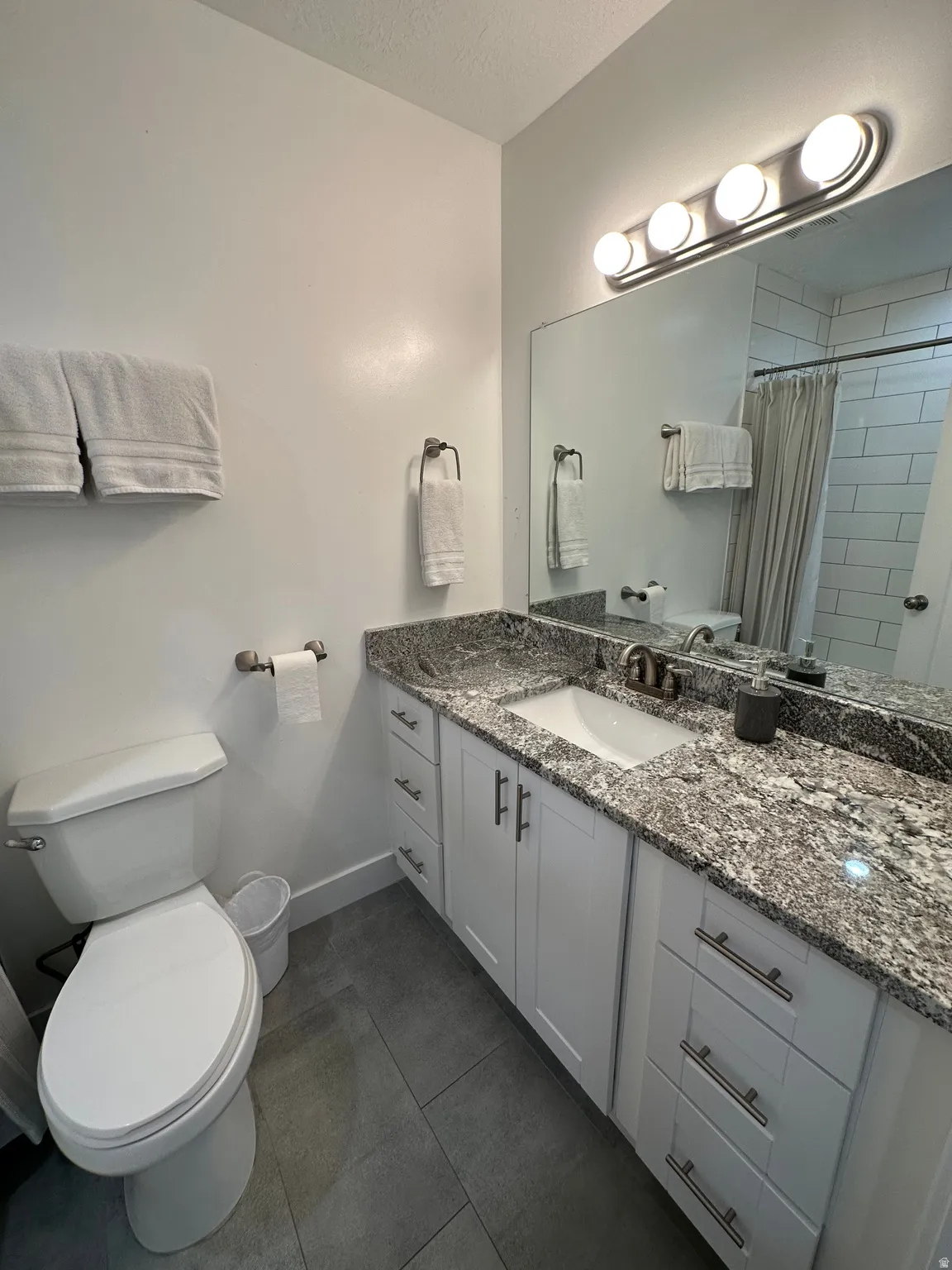 Full bath with vanity, tiled shower, a textured ceiling, and dark tile patterned floors