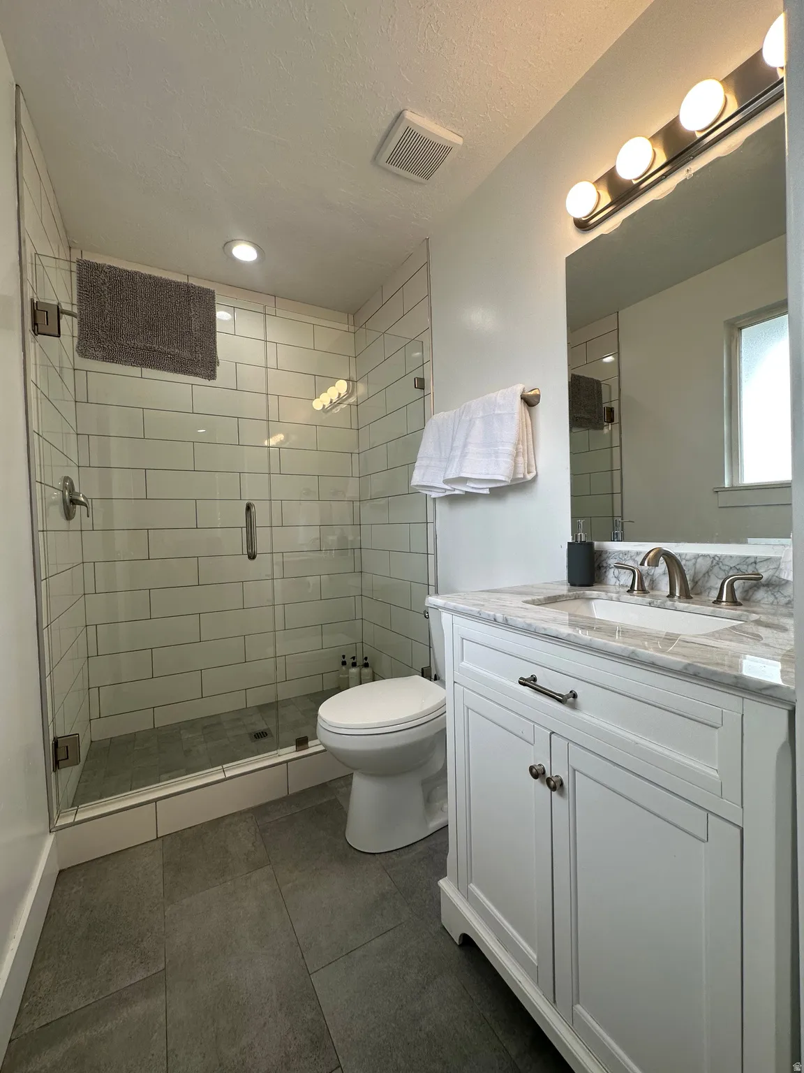 Full bath featuring vanity, a stall shower, dark tile patterned flooring, and a textured ceiling