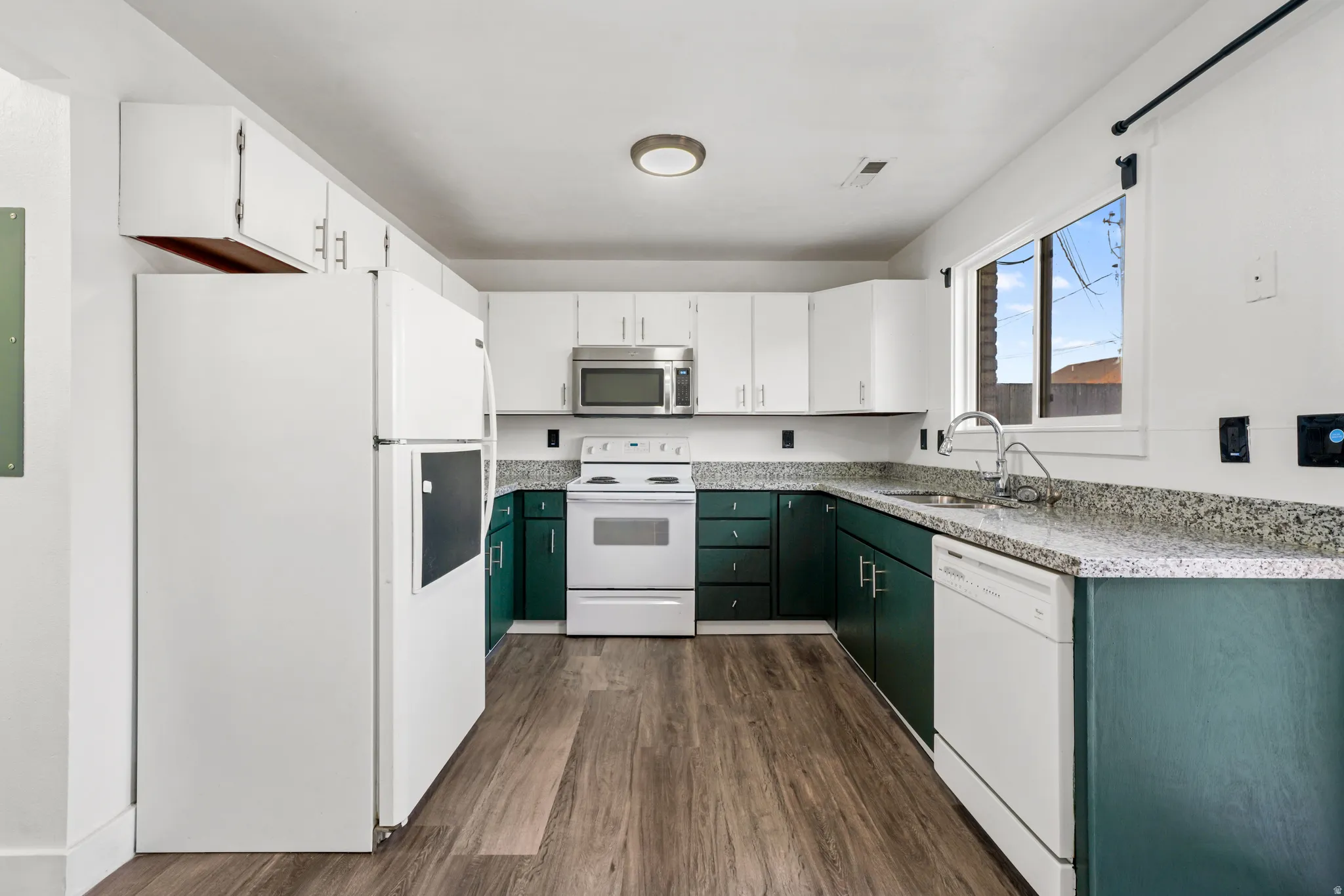 Kitchen with dual tone cabinetry, white appliances, and dark wood-style flooring