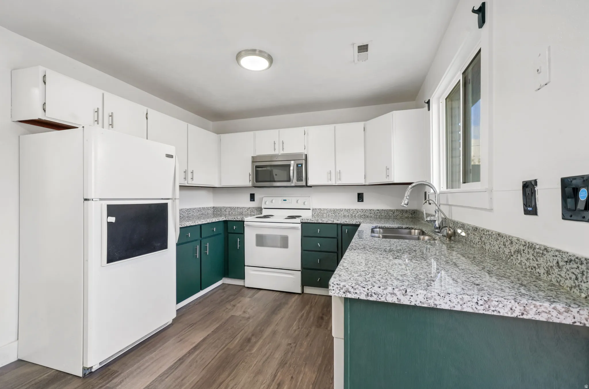 Kitchen with dual tone cabinetry, white appliances, light stone countertops, and dark wood-type flooring