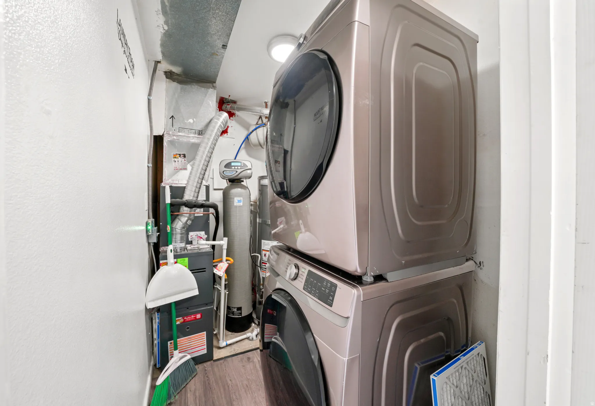 Laundry area with stacked washing machine and dryer, heating unit, and wood finished floors