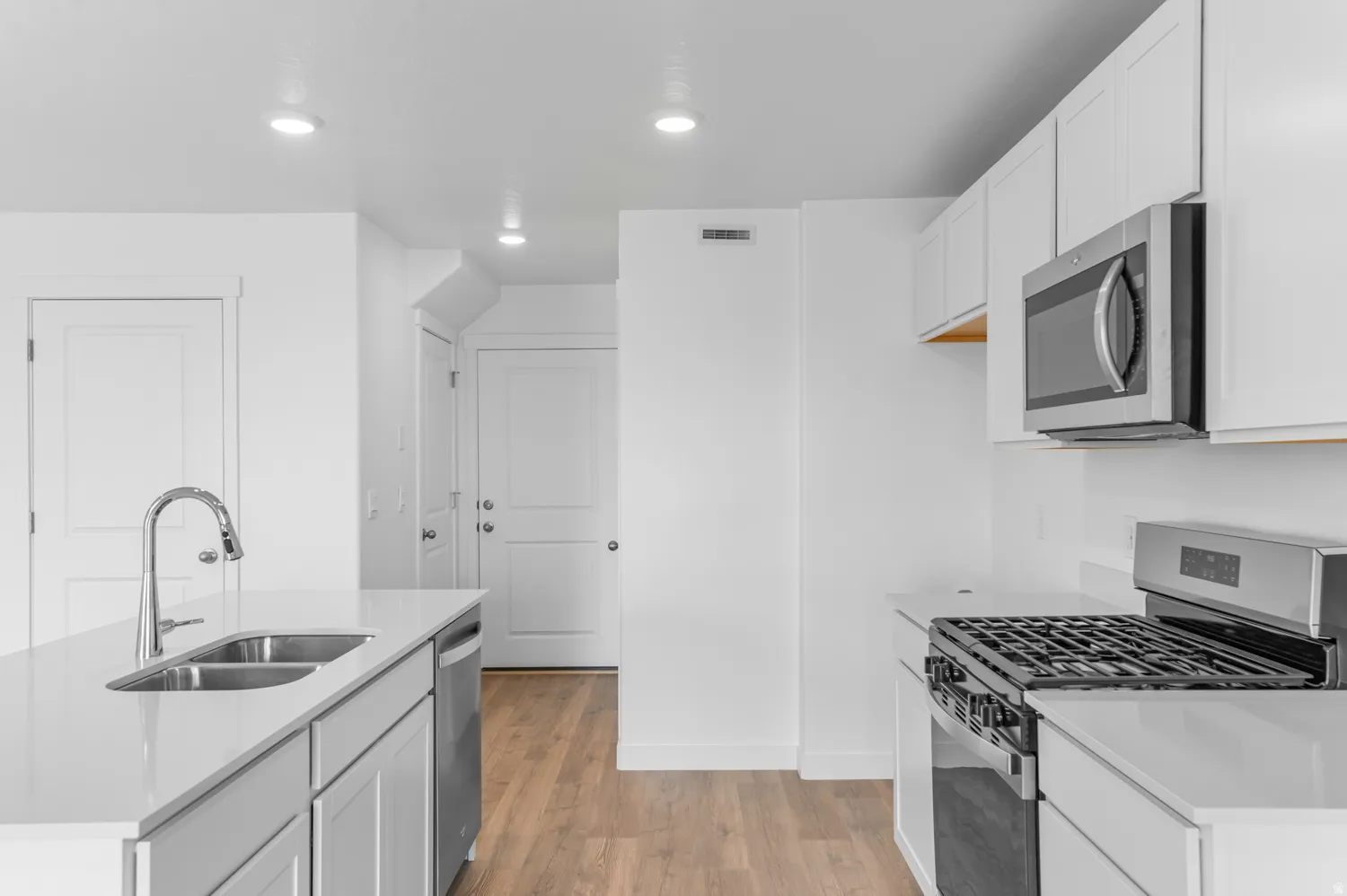 Kitchen featuring stainless steel appliances, white cabinetry, light wood-type flooring, recessed lighting, and light stone counters