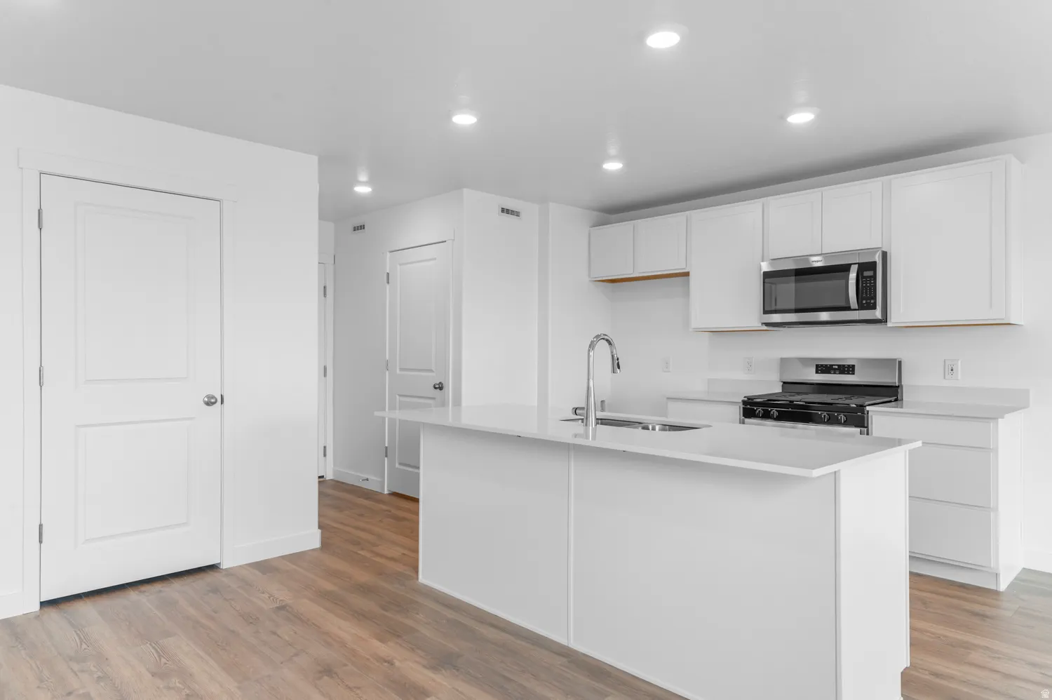 Kitchen with white cabinets, stainless steel appliances, light wood-style flooring, a kitchen island with sink, and recessed lighting