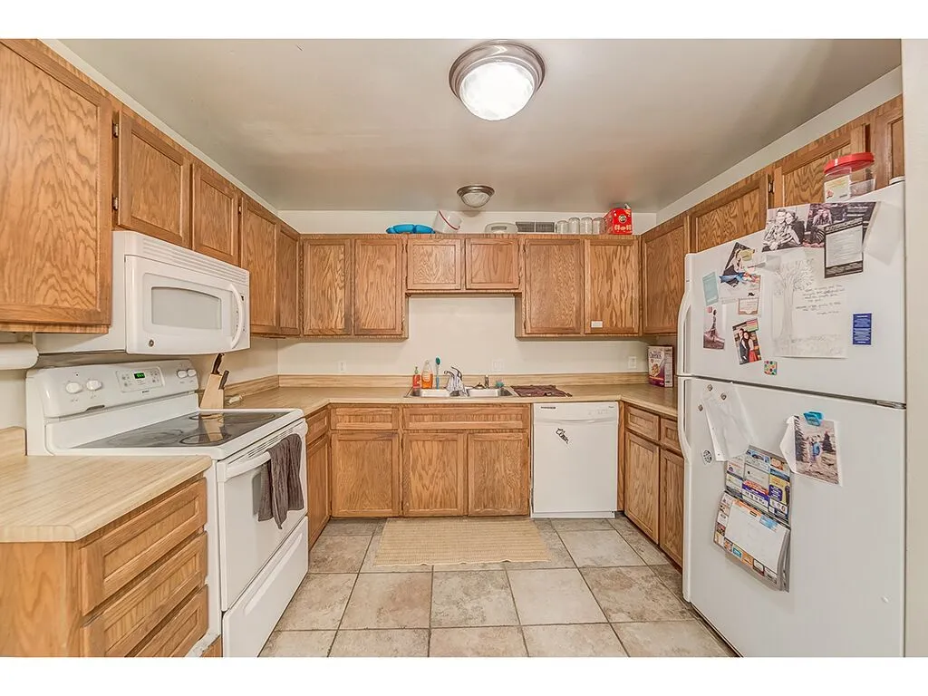 Kitchen featuring white appliances, light countertops, wood finish cabinets, and light tile patterned floors