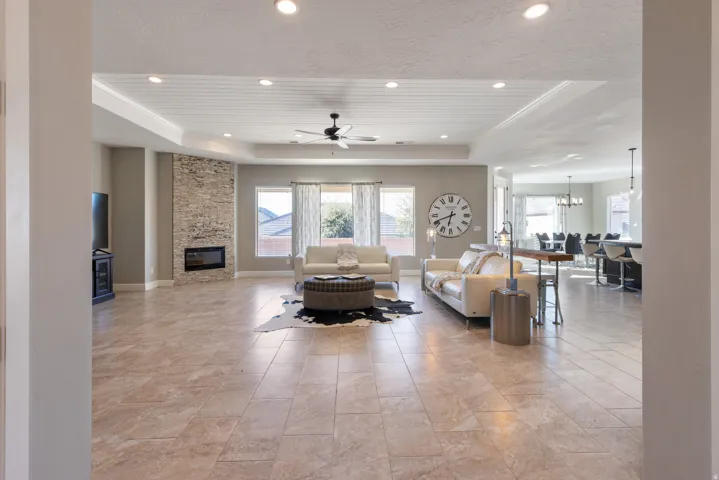 Living room with a ceiling fan, a fireplace, a tray ceiling, and a chandelier