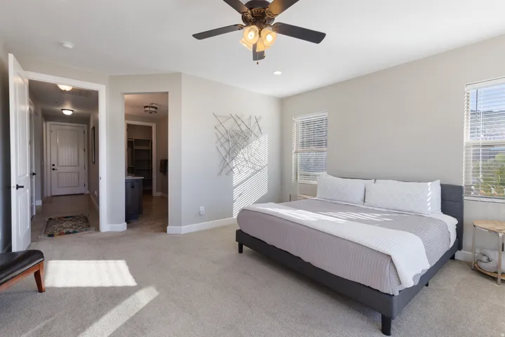 Bedroom with a walk in closet, light colored carpet, multiple windows, a ceiling fan, and recessed lighting