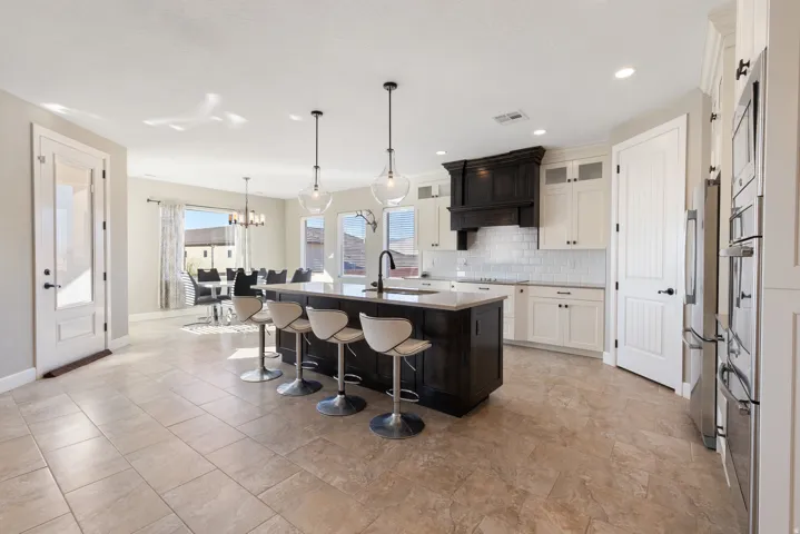 Kitchen with a kitchen breakfast bar, glass insert cabinets, a center island with sink, a chandelier, and hanging light fixtures