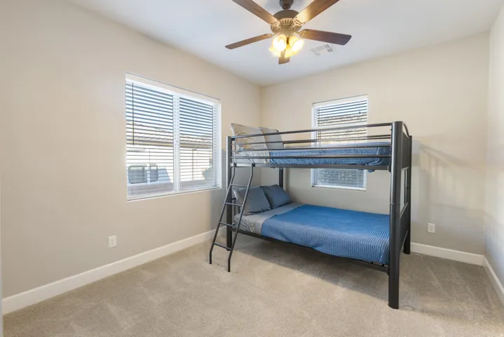 Bedroom with light colored carpet, multiple windows, and ceiling fan