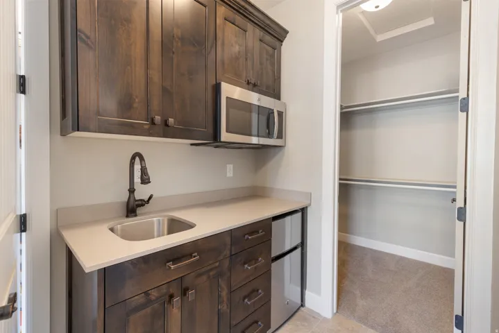 Kitchen featuring dark brown cabinetry, appliances with stainless steel finishes, light carpet, and light stone counters