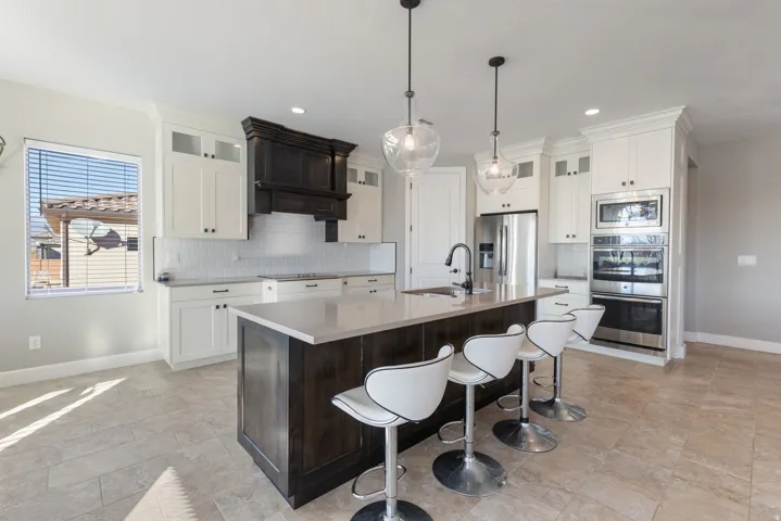 Kitchen with glass insert cabinets, dark brown cabinetry, a kitchen island with sink, appliances with stainless steel finishes, and a kitchen bar