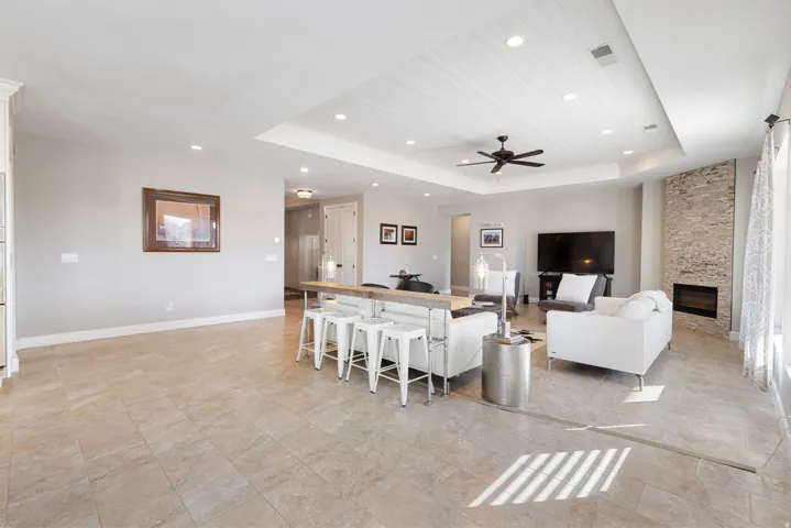 Living area with a raised ceiling, a stone fireplace, ceiling fan, and recessed lighting