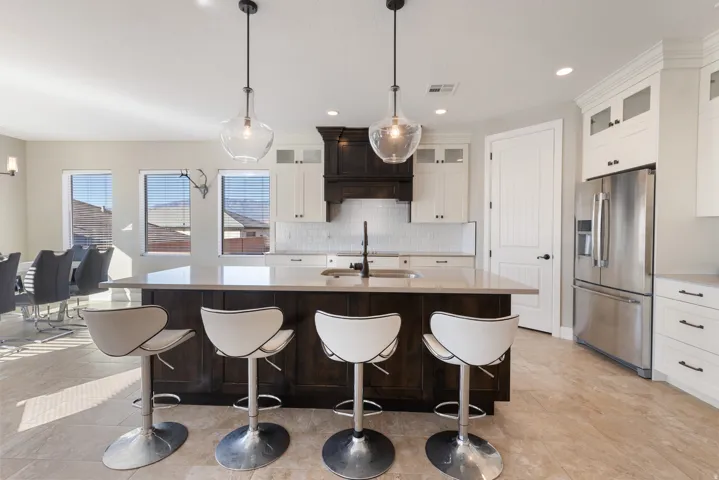 Kitchen with glass insert cabinets, stainless steel refrigerator with ice dispenser, an island with sink, a breakfast bar, and recessed lighting