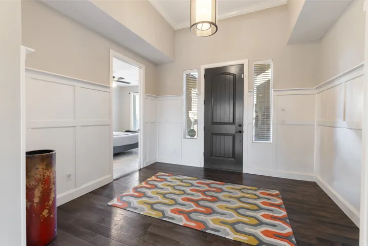 Foyer entrance featuring a decorative wall, dark wood-type flooring, crown molding, a ceiling fan, and wainscoting