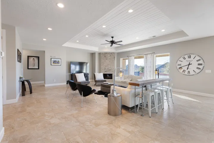 Living area with a raised ceiling, a fireplace, ceiling fan, and recessed lighting