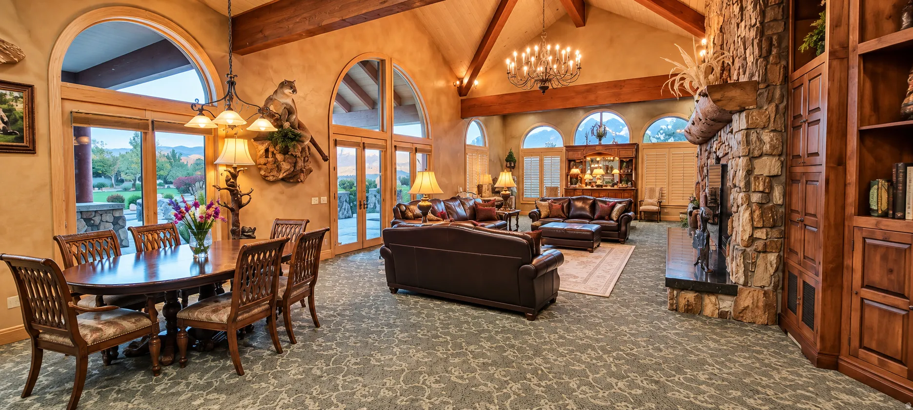 Vaulted ceilings with exposed wood beams, arched windows, built-in shelving, stone fireplace, and wood-finish flooring