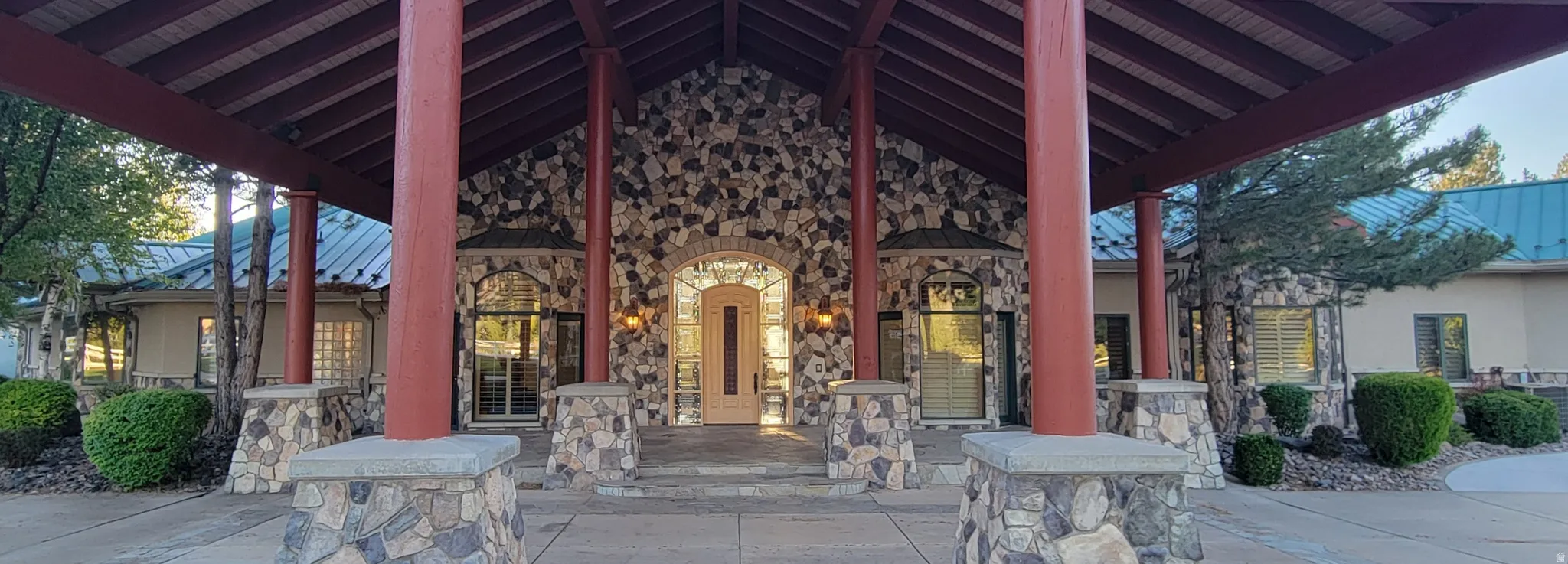 Stone veneer exterior with an arched entryway, covered portico, substantial columns, and a metal roof