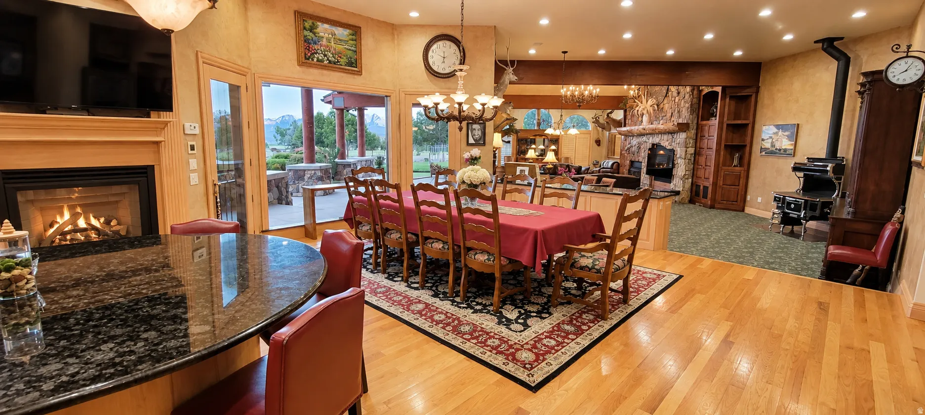 Hardwood flooring throughout, a gas fireplace with a wood mantle, an adjacent dining area with chandelier lighting, a stone-clad hearth, and a built-in wood-burning stove