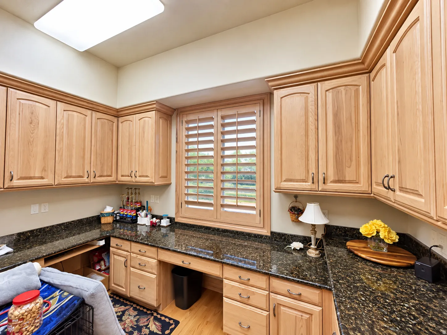 Recessed lighting, wood-finish cabinetry, dark speckled countertops, built-in desk area, and wood-finish window shutters