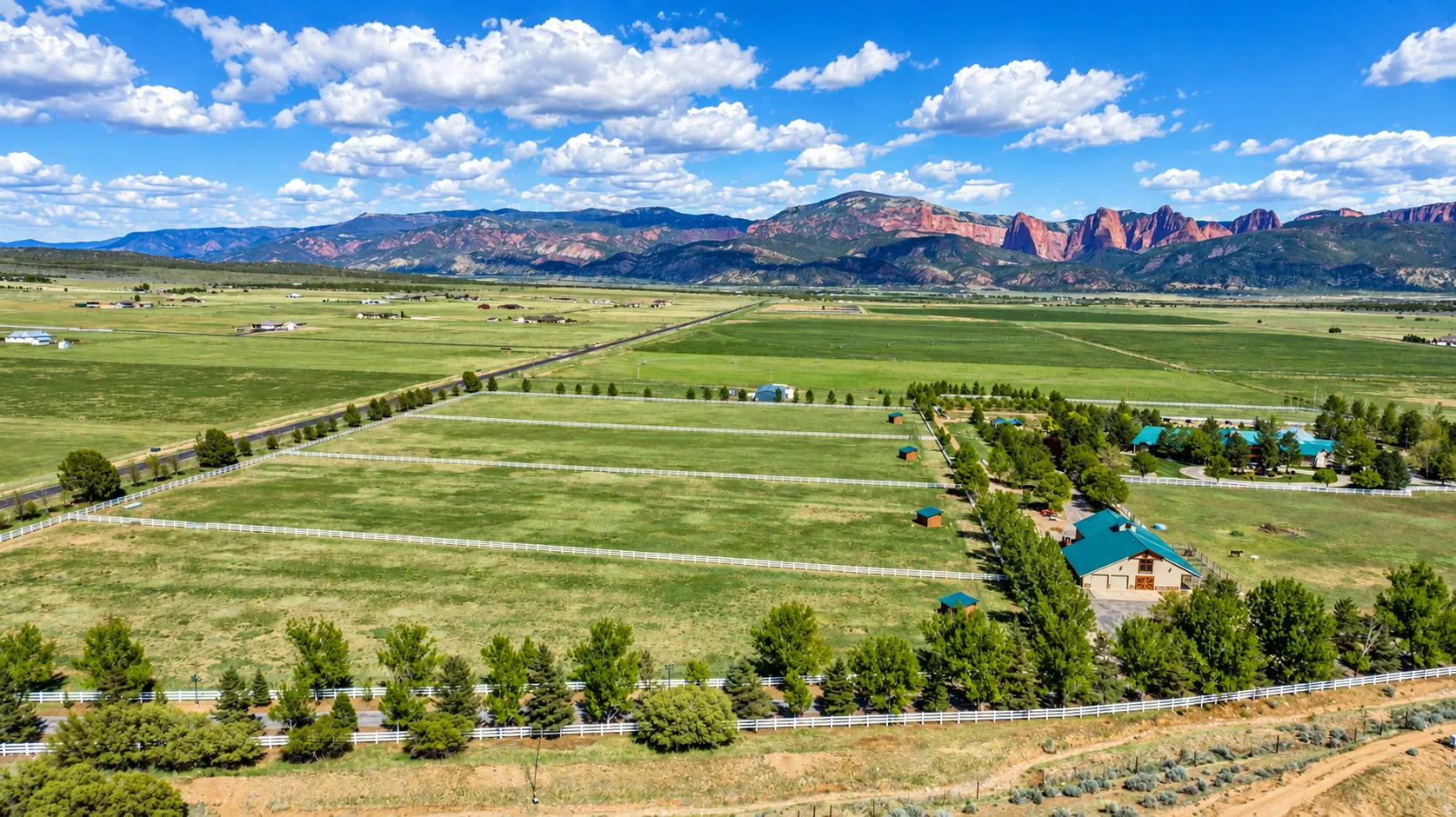 Expansive acreage with multiple structures, white fencing, and mature tree lines