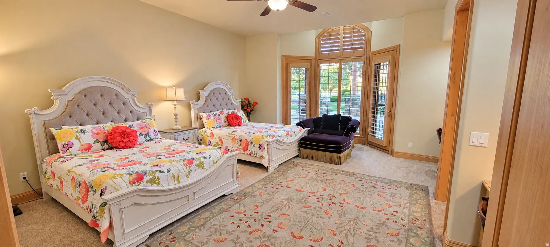 Arched window with plantation shutters, wood-finish doors, ceiling fan, and neutral carpet flooring
