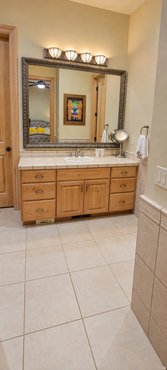 Extended vanity with wood cabinetry, tiled countertop, and an integrated sink