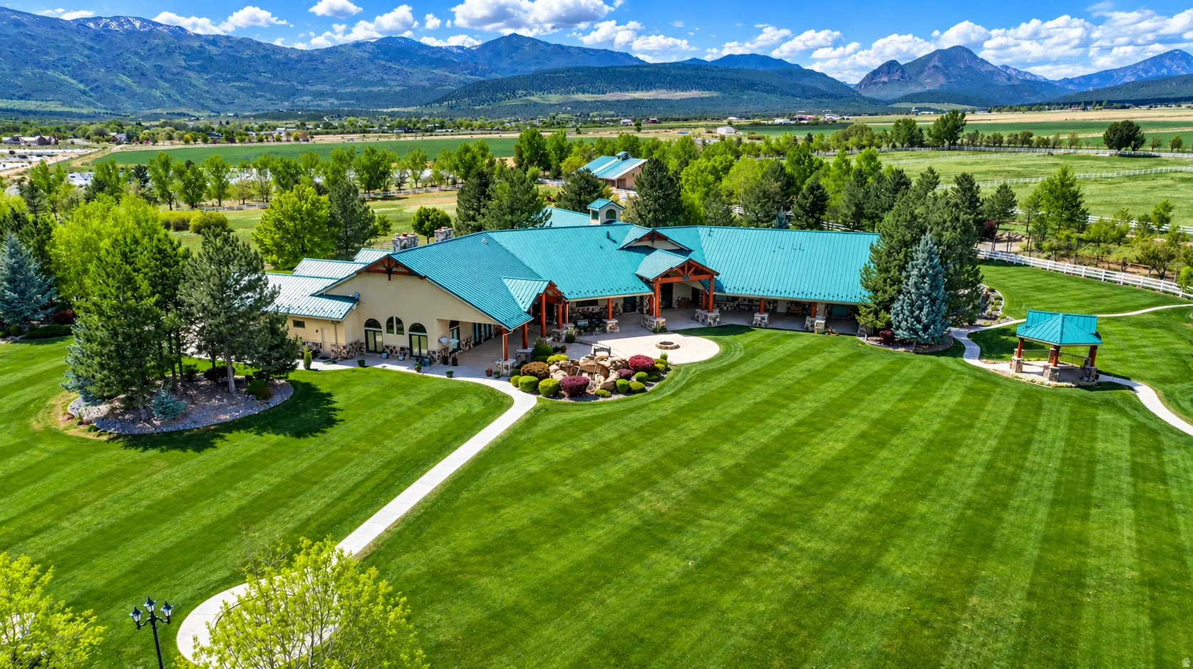Expansive green lawn, extensive patio area, mature trees, mountain backdrop, and an outdoor gazebo