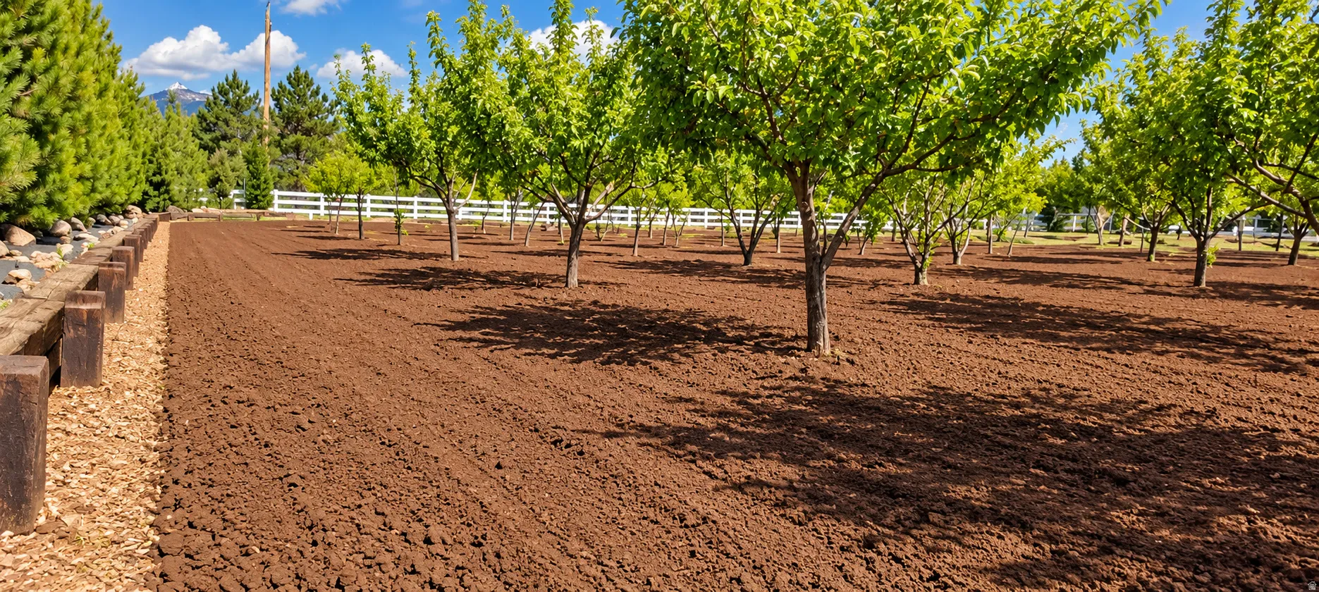 Cultivated land featuring multiple mature trees and a white fence