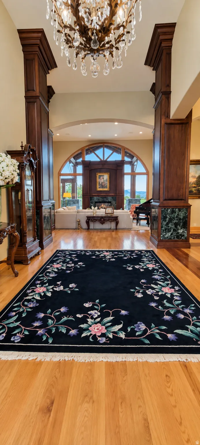 Hardwood flooring with a polished finish, decorative ceiling-mounted chandelier, and substantial wood-paneled columns with marble accents