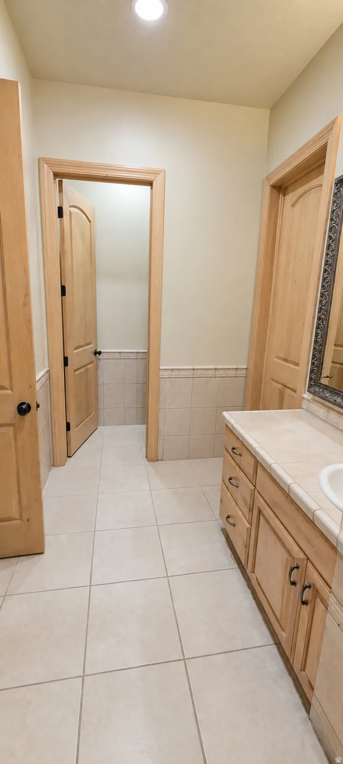 Light-toned tile flooring, light wood-finish cabinetry with dark hardware, recessed lighting, and a built-in vanity with an integrated sink