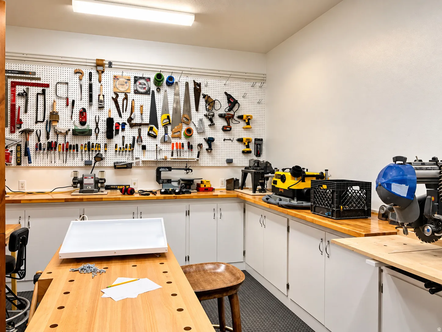 Workroom featuring extensive built-in cabinetry, wood-finish countertops, pegboard organization, and overhead fluorescent lighting