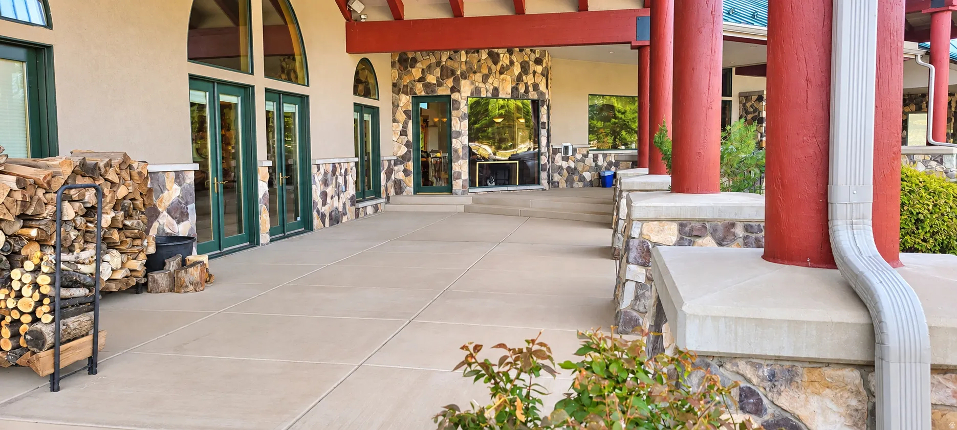 Expansive outdoor patio with stone veneer accents, multiple arched windows, red structural columns, and a built-in outdoor fireplace