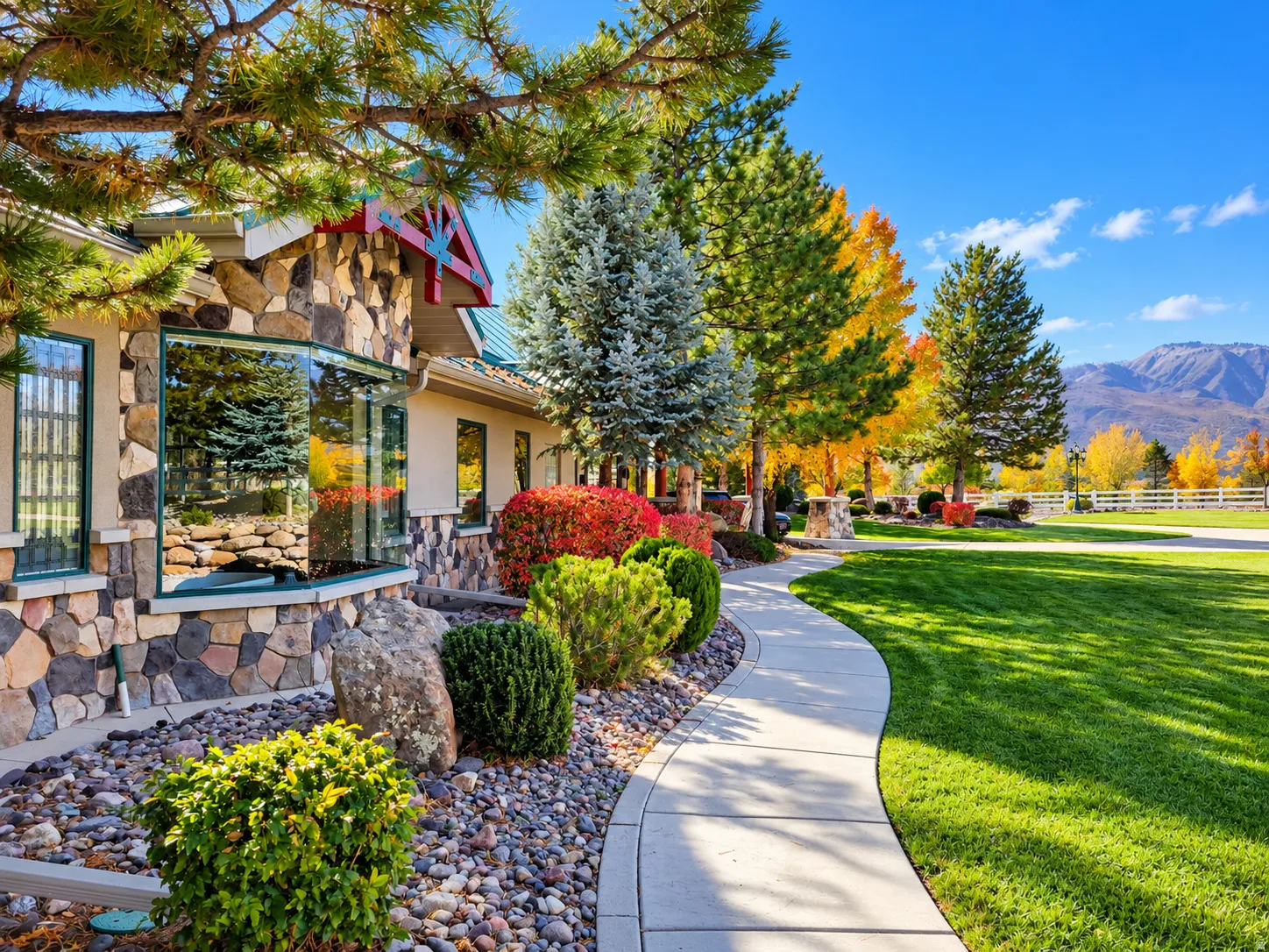 Stone facade with a bay window, manicured lawn, paved walkway, and mature landscaping