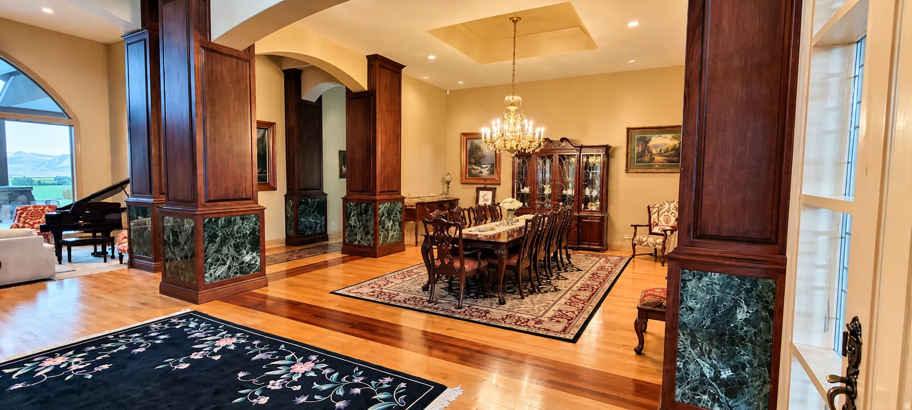 Hardwood flooring, decorative wood columns with stone accents, arched doorways, recessed ceiling detail, and a chandelier