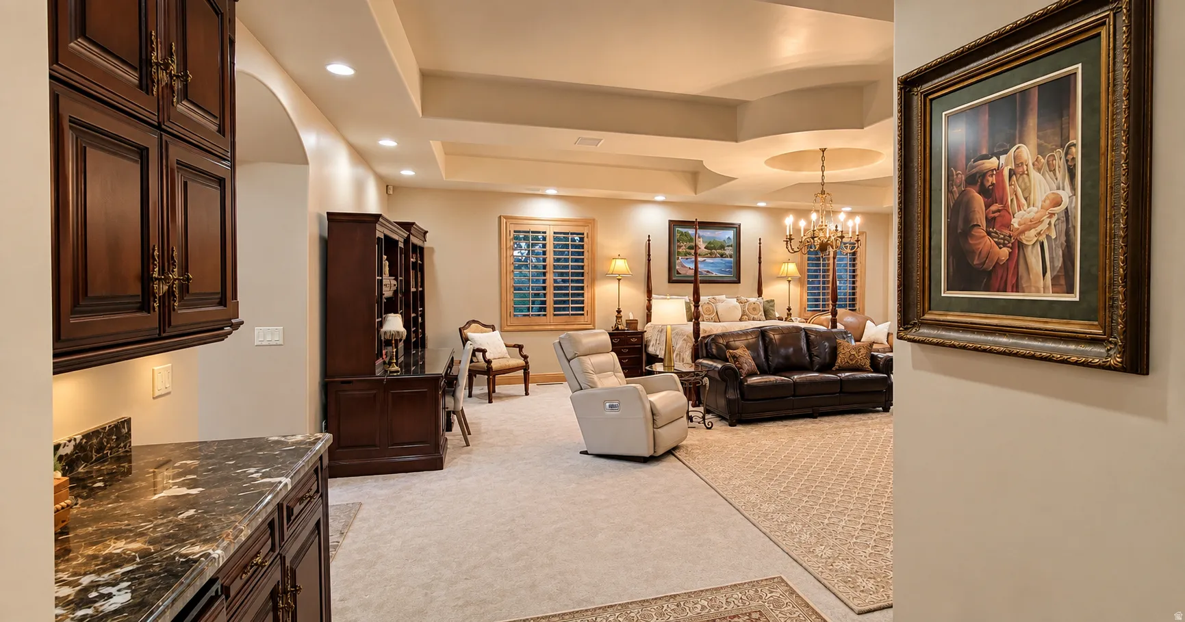 Tray ceiling with recessed lighting, dark wood-finish cabinetry with stone countertop, plantation shutters, and chandelier