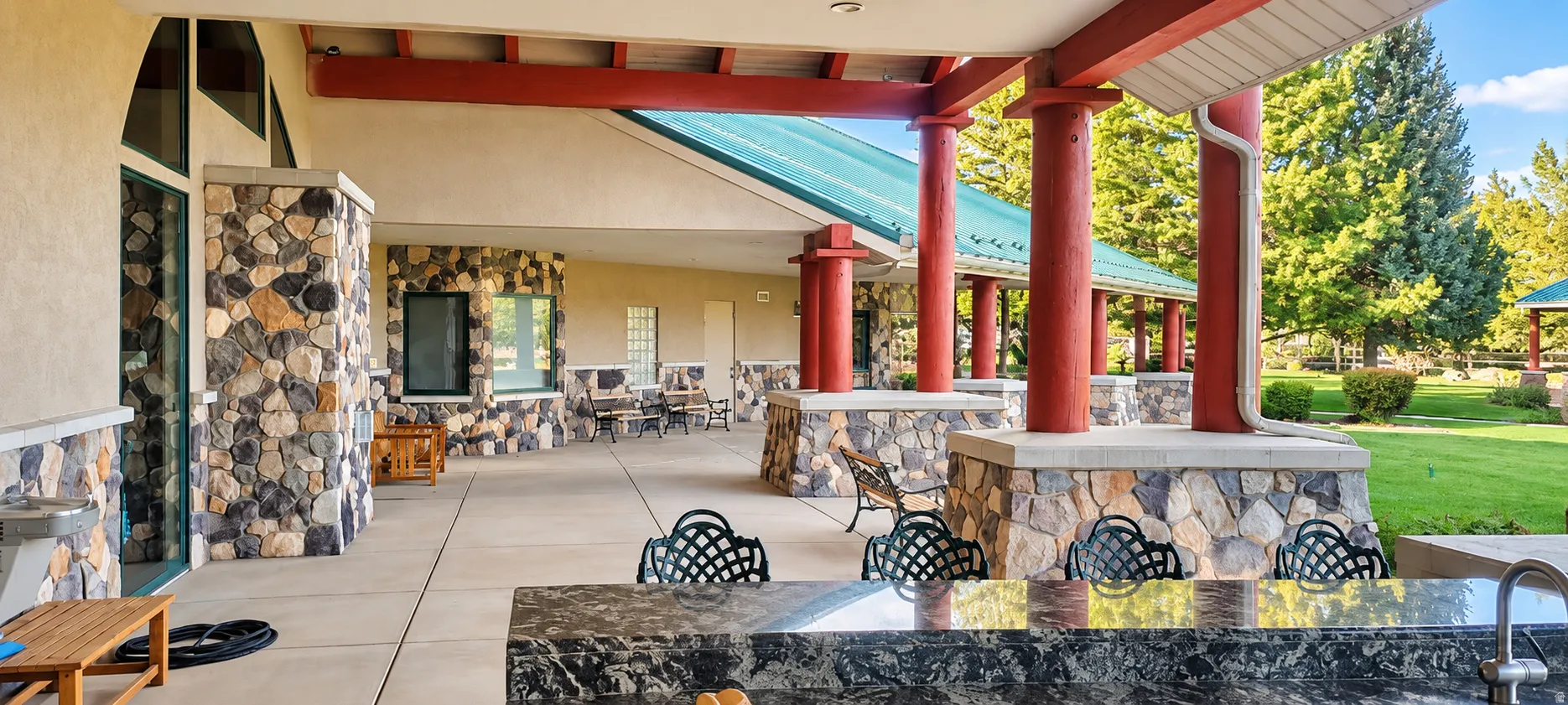 Expansive covered patio featuring stone-clad columns, a built-in outdoor bar with a dark stone-finish countertop, and a green metal roof