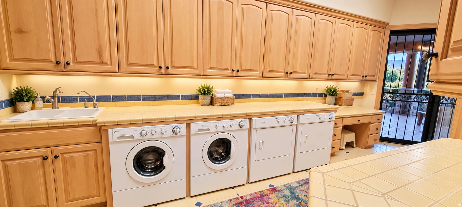 Extensive light wood cabinetry with black hardware, tile countertops, and a double basin sink