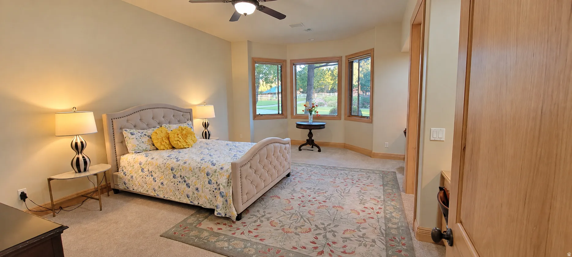 Bay window with wood trim, ceiling fan, carpet flooring, and light wall finishes