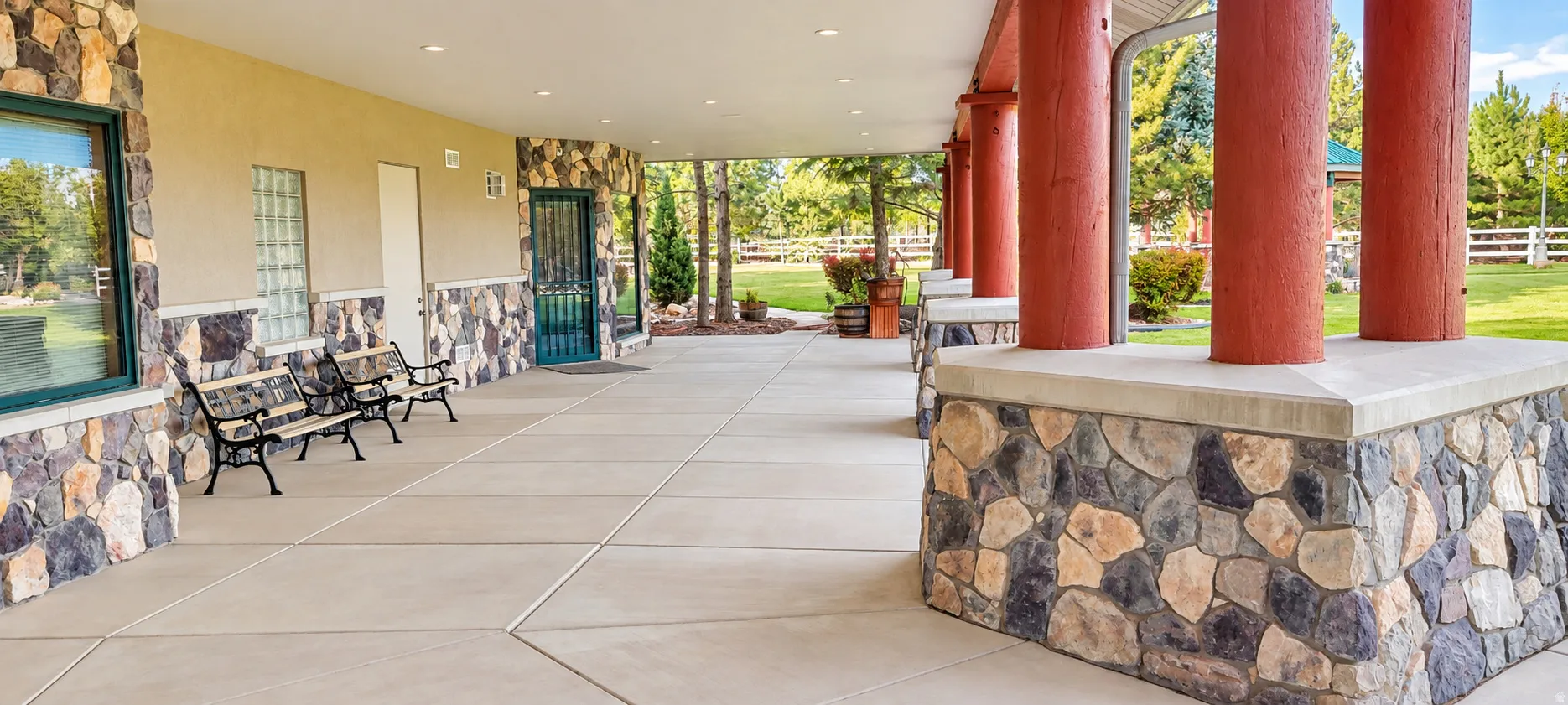 Expansive covered patio featuring a concrete surface, stone base walls, and substantial support columns