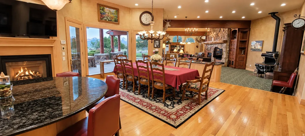 Hardwood flooring throughout, a gas fireplace with a wood mantle, an adjacent dining area with chandelier lighting, a stone-clad hearth, and a built-in wood-burning stove