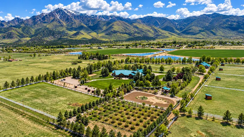 Expansive property featuring multiple structures, cultivated fields, a riding arena, and a mountainous backdrop