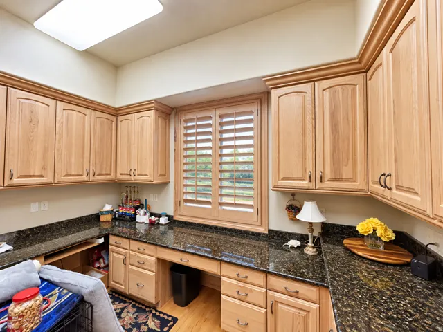 Recessed lighting, wood-finish cabinetry, dark speckled countertops, built-in desk area, and wood-finish window shutters