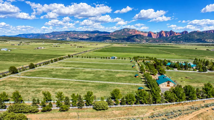 Expansive acreage with multiple structures, white fencing, and mature tree lines