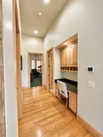 Hallway featuring wood-finish flooring, recessed lighting, built-in desk with stone countertop, and custom cabinetry