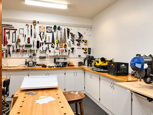 Workroom featuring extensive built-in cabinetry, wood-finish countertops, pegboard organization, and overhead fluorescent lighting